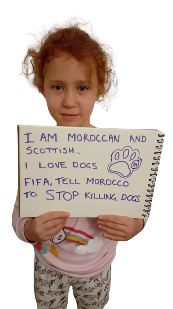 Young girl with red hair looks into camera holding a sign saying 'I am Moroccan and Scottish, I love dogs. Fifa, tell Morocco to stop killing dogs.